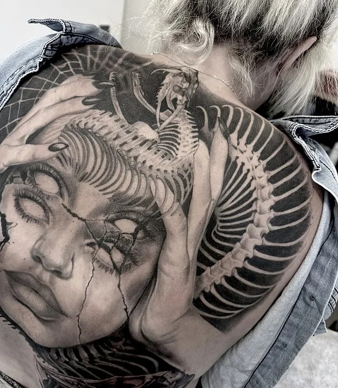 Large black-and-grey tattoo on a woman's back featuring a skull and snake.