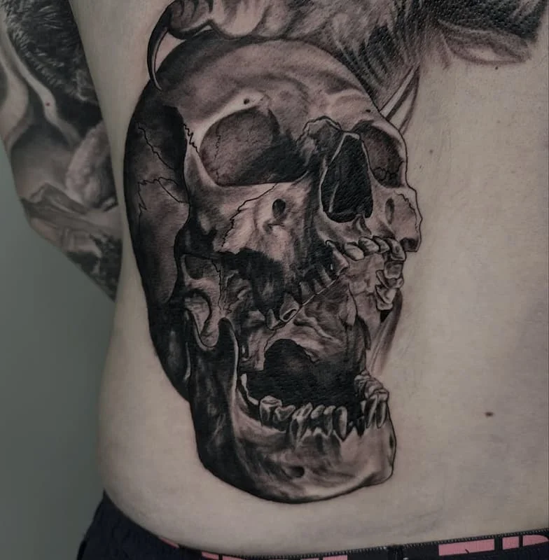 Detailed black-and-grey skull tattoo on rib.