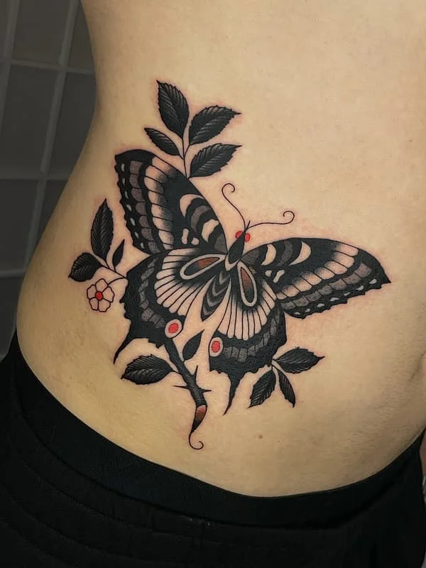 Blackwork butterfly tattoo on rib with floral elements.