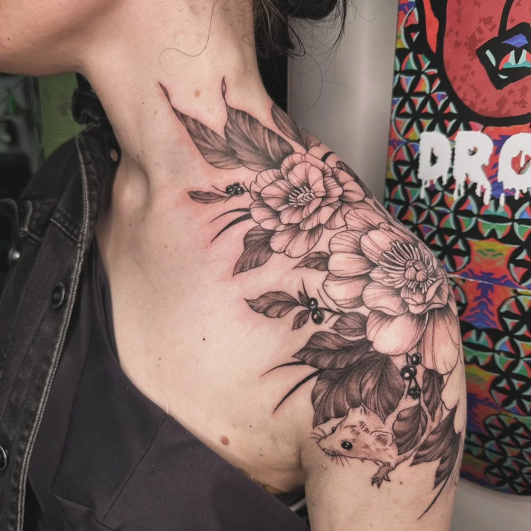 Illustrative black-and-grey tattoo of flowers and a mouse on shoulder.