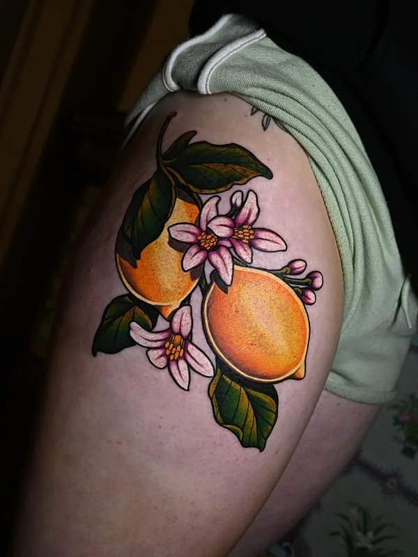 Colorful thigh tattoo of lemons and flowers.