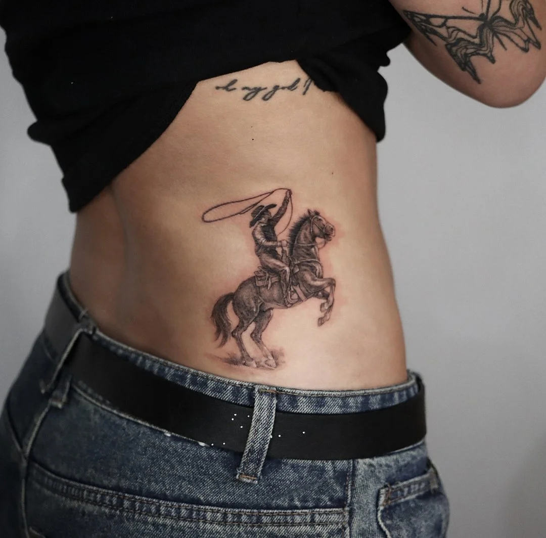 Illustrative cowboy tattoo on rib with horse rearing.