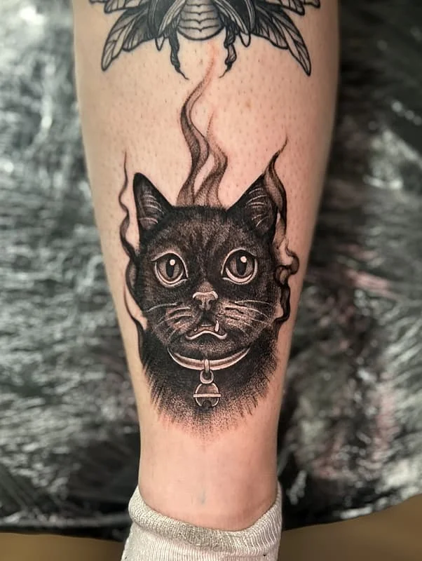 Black-and-grey tattoo of a cat with flames on calf.