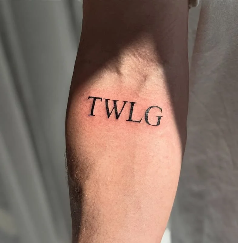 Minimalist blackwork tattoo of initials 'TWL' on forearm.