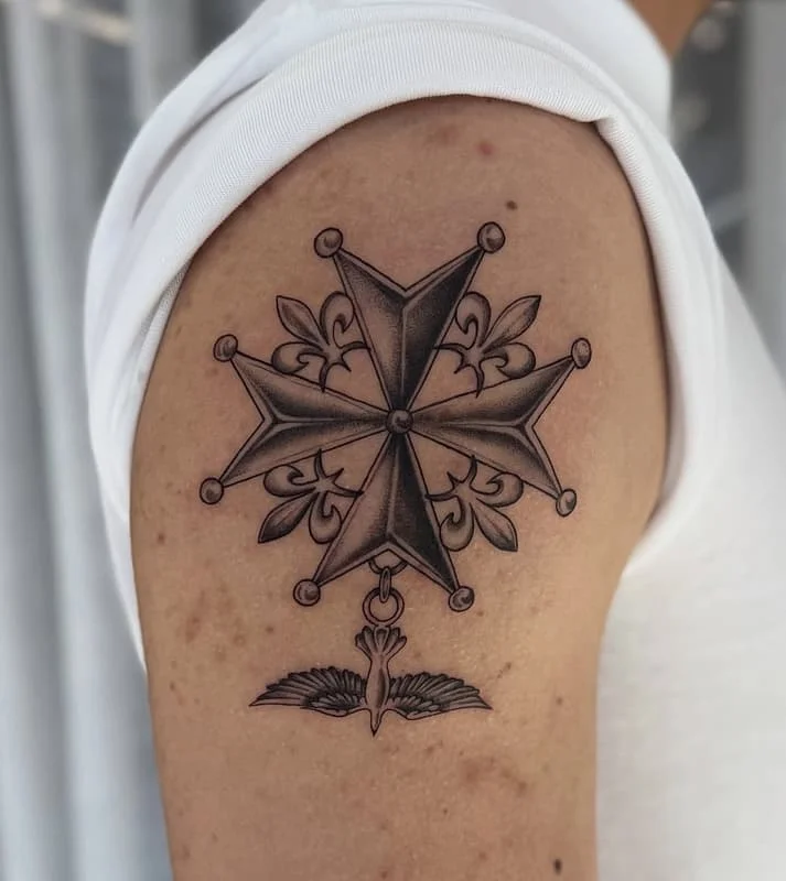 Black-and-grey cross tattoo with floral and bird elements on upper arm.
