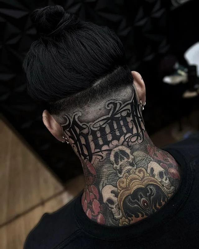 Intricate blackwork neck and back tattoo featuring skulls and script.