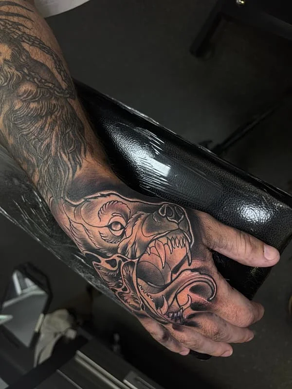 Detailed black-and-grey wolf tattoo on hand and forearm.