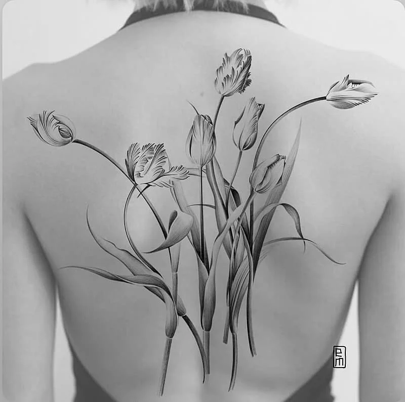Realistic black-and-grey floral tattoo on a woman's back.