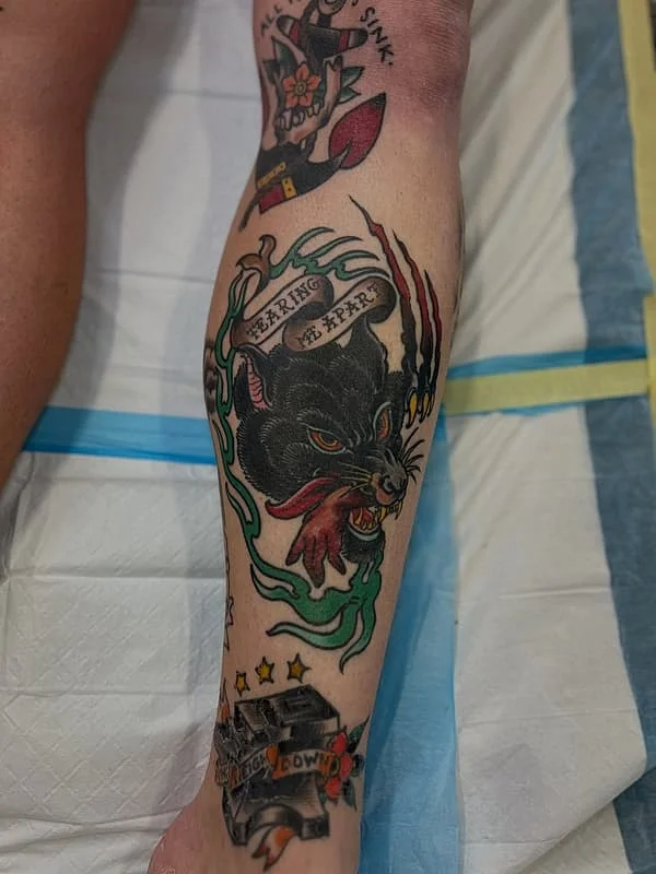 Traditional tattoo of a black cat with claws and flames on leg.