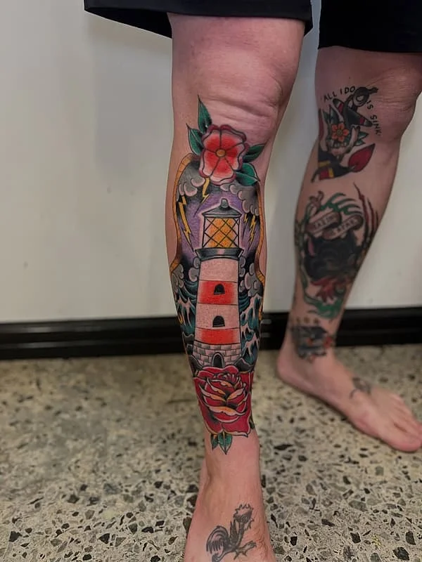 Colorful lighthouse tattoo on a calf with flowers and waves.