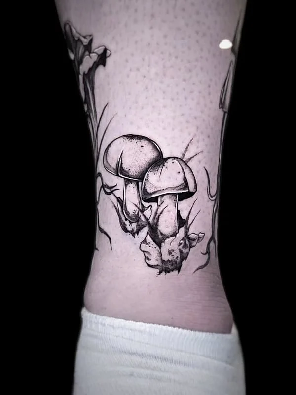 Black and grey illustrative tattoo of mushrooms on a leg