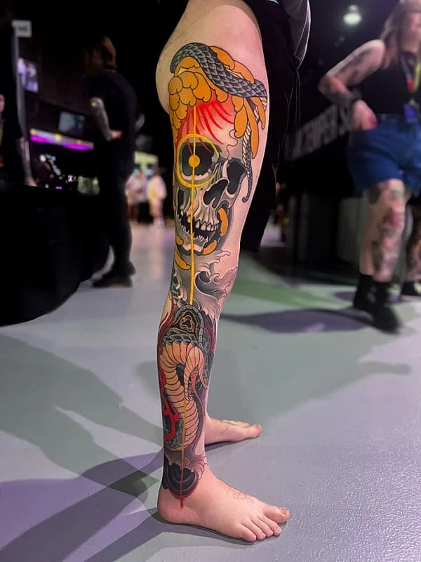 Colorful leg tattoo of a skull with a snake and flowers.