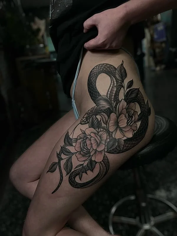 Thigh tattoo of a snake and flowers in blackwork style.