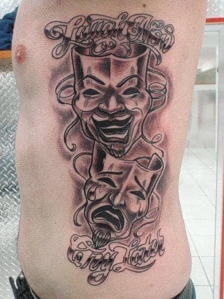 Large black-and-grey comedy and tragedy masks tattoo on rib.