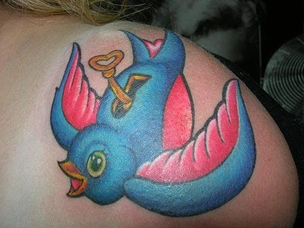 Colorful bird tattoo with a key on shoulder.