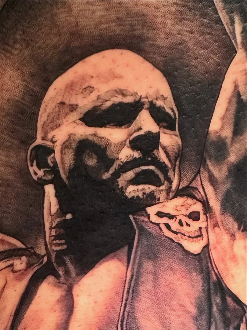 Realistic tattoo of a muscular man with a skull on the arm.