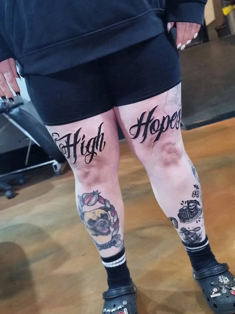 Large script tattoo saying 'High Hopes' on thighs.