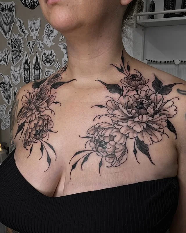 Large black and grey floral tattoo on chest and shoulders.