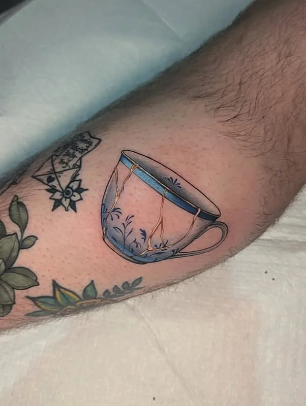 Illustrative watercolor tattoo of a teacup on forearm.