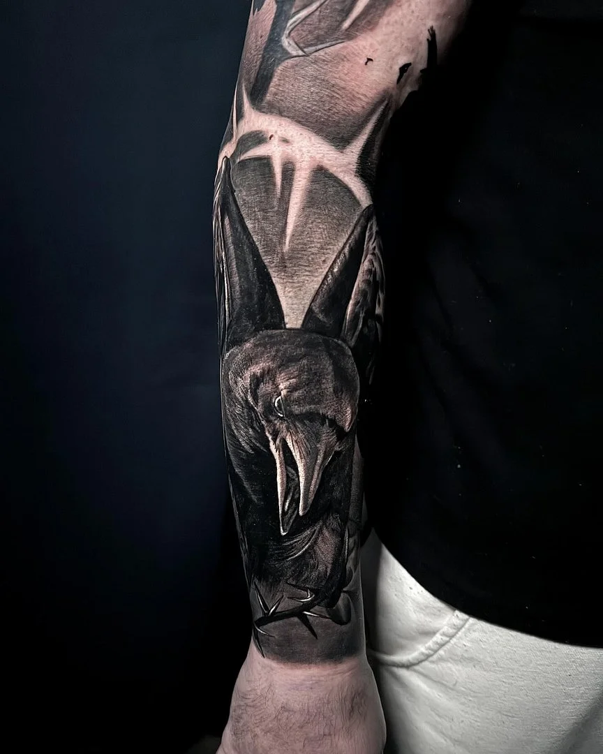 Detailed black-and-grey bird tattoo on forearm.