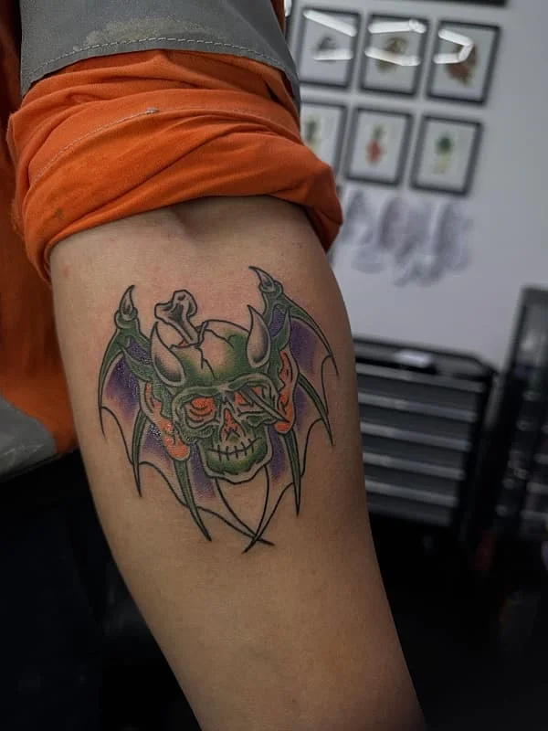 Colorful skull tattoo with wings on arm.
