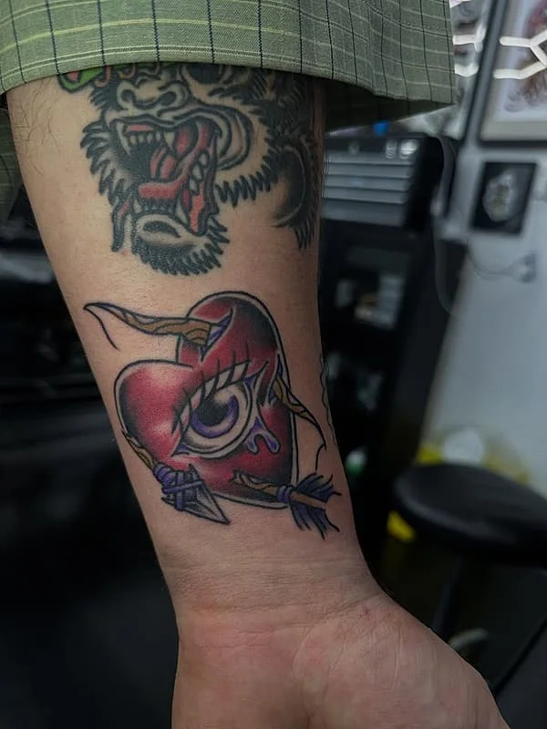 Colorful traditional heart tattoo with an eye and arrow.