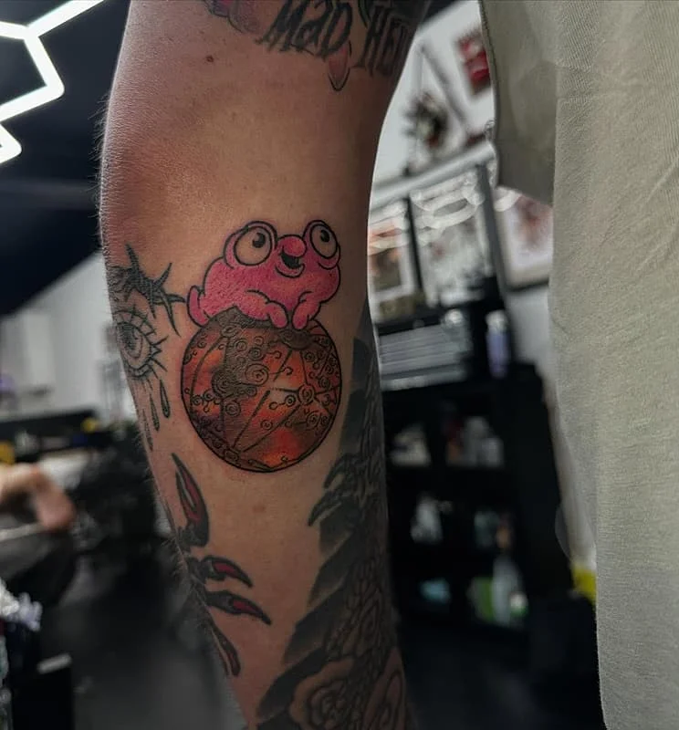 Colorful frog tattoo on forearm sitting on a planet.