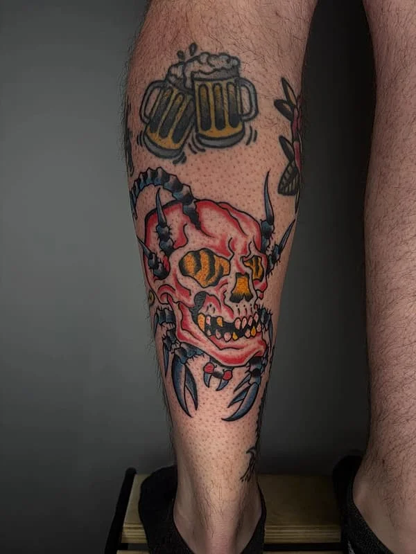 Colorful skull tattoo with claws and beer on calf.