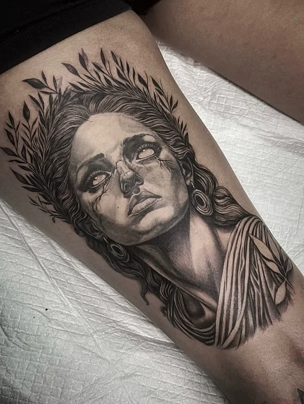 Realistic black-and-grey tattoo of a woman on thigh.