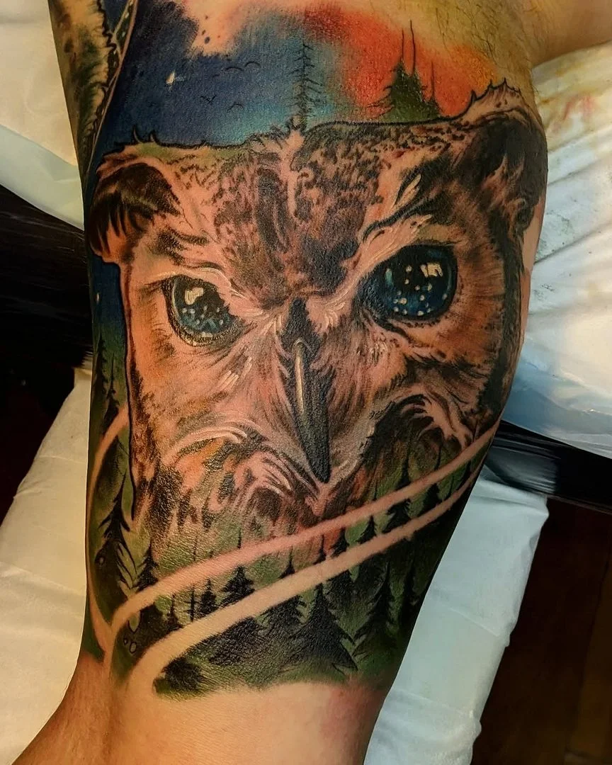 Colorful owl tattoo with nature elements on thigh.