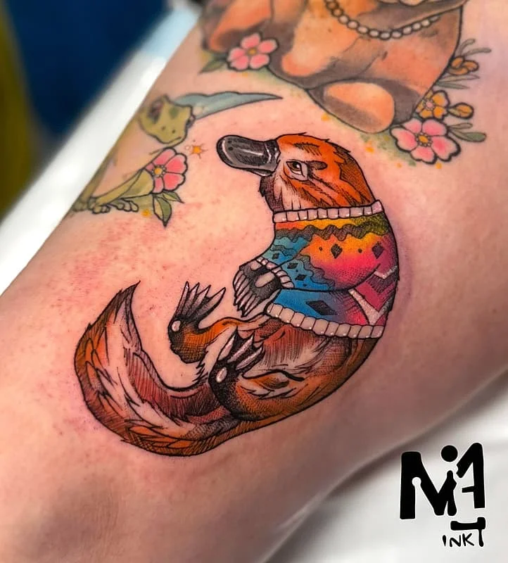 Colorful platypus tattoo on forearm wearing a sweater.