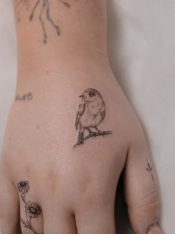 Fine-line tattoo of a bird on a hand.