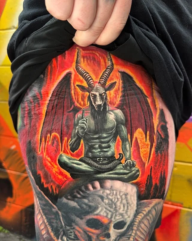 Colorful thigh tattoo of a demon with skulls and fire.