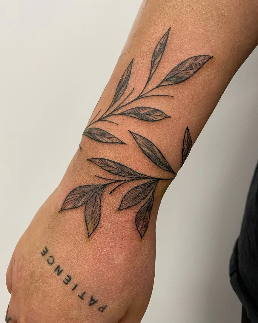 Minimalist fine-line tattoo of leaves on forearm.