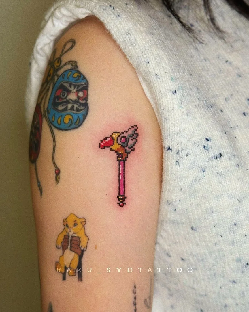 Small pixel-art magic wand tattoo on arm.