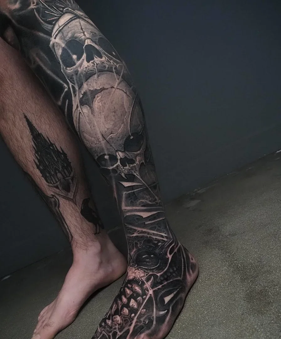 Large black-and-grey biomechanical skull tattoo on leg.