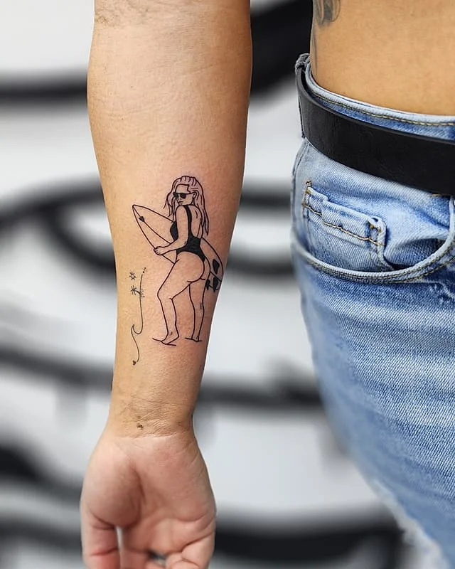 Illustrative tattoo of a surfer girl on forearm.