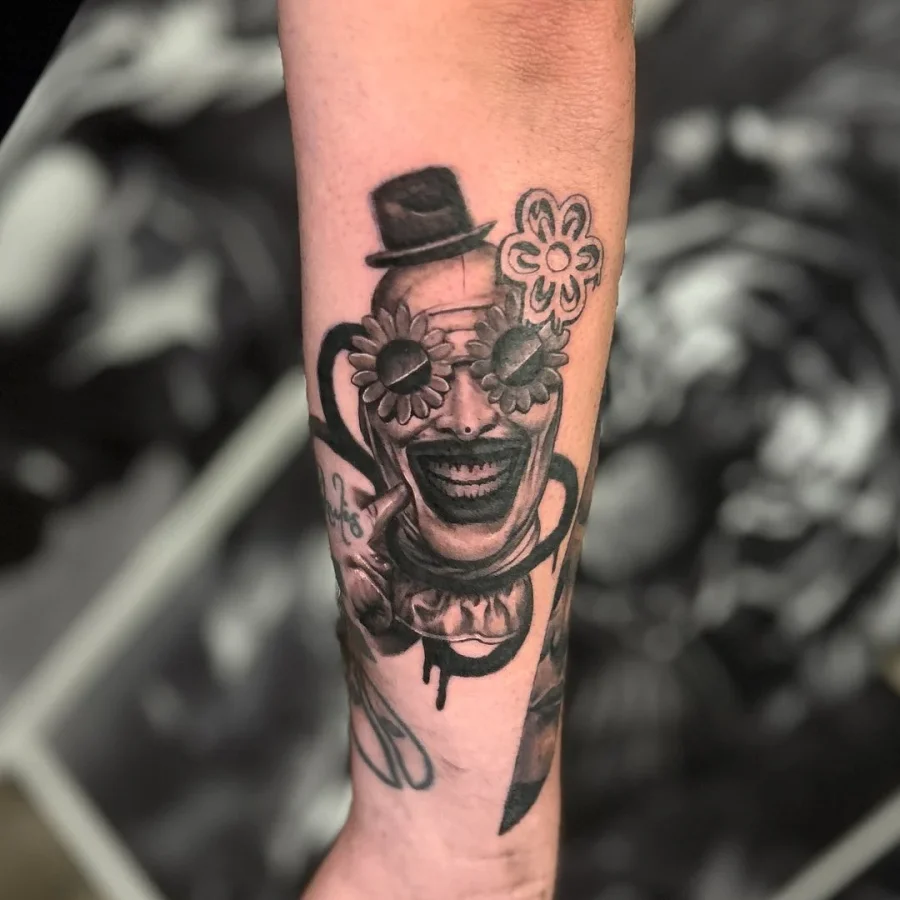 Black and grey clown tattoo with flowers on forearm