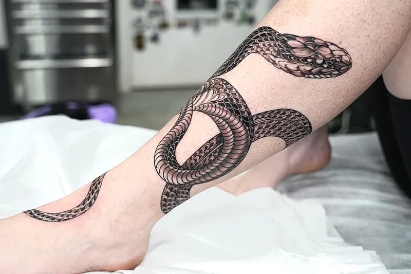 Realistic black-and-grey snake tattoo on calf.