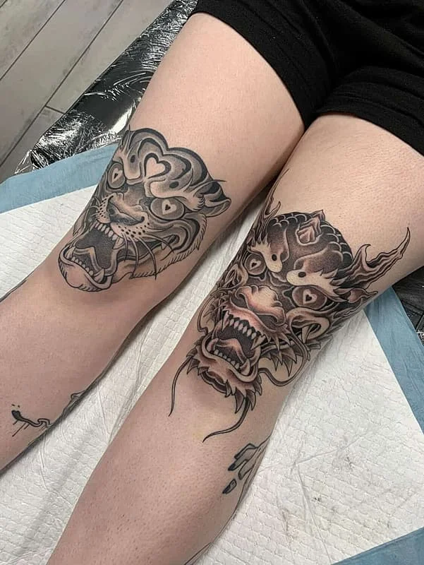 Large black-and-grey dragon and lion tattoo on leg.