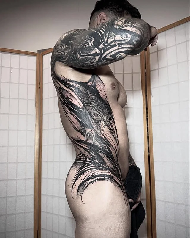 Large blackwork biomechanical tattoo on male arm and rib.