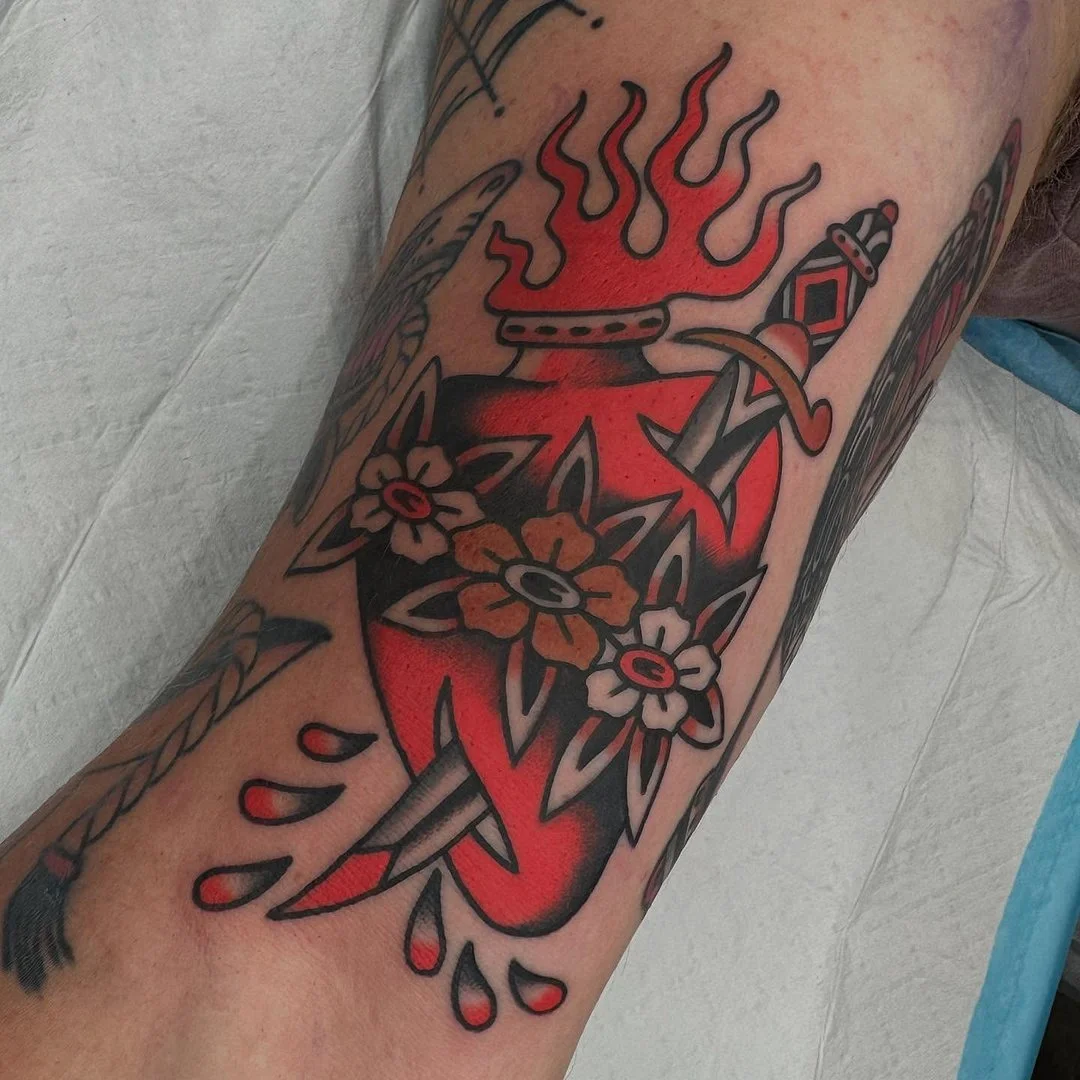 Traditional tattoo of a heart with flowers and a sword.