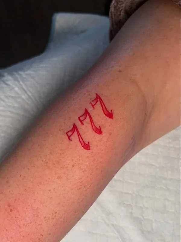 Minimalist tattoo of the number 777 on forearm.