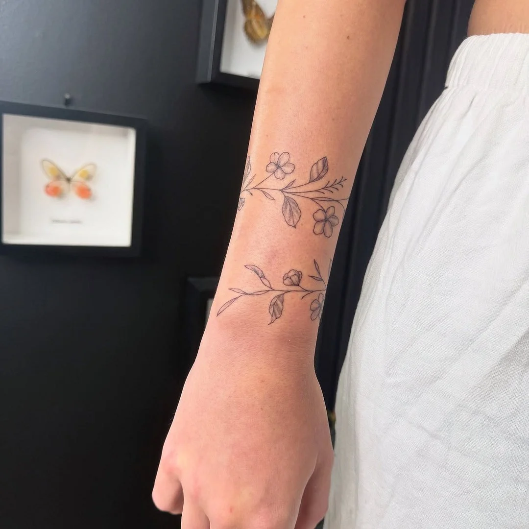 Delicate fine-line floral tattoo on forearm.