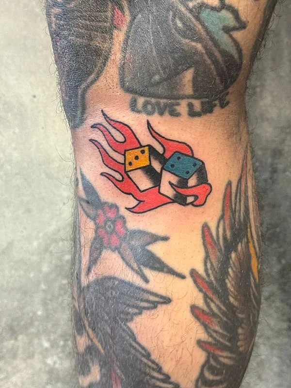 Colorful dice tattoo with flames on an arm.