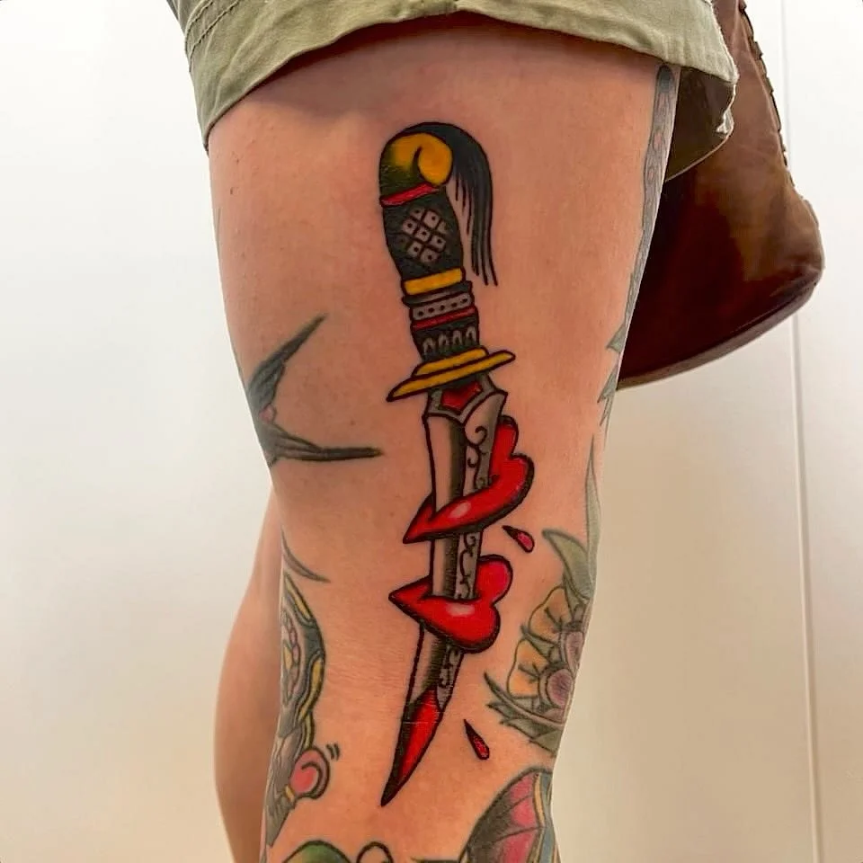 Traditional dagger tattoo with blood and roses on leg.