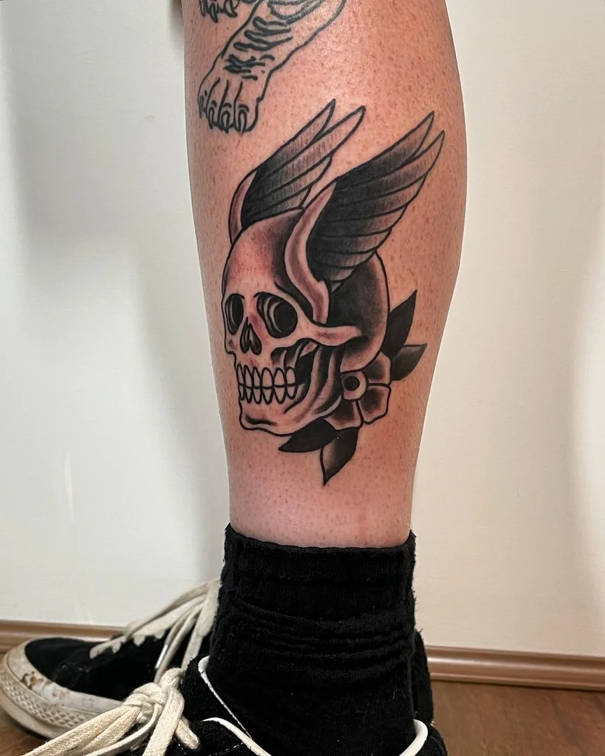 Black-and-grey skull tattoo with wings on calf.