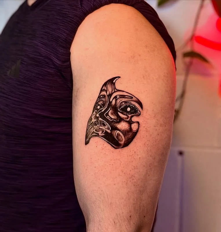 Abstract black-and-grey face tattoo on upper arm.