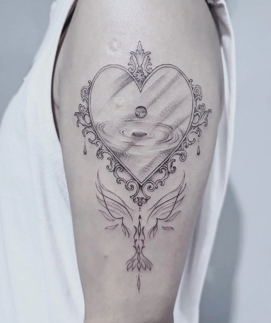 Fine-line heart tattoo with wings on upper arm.