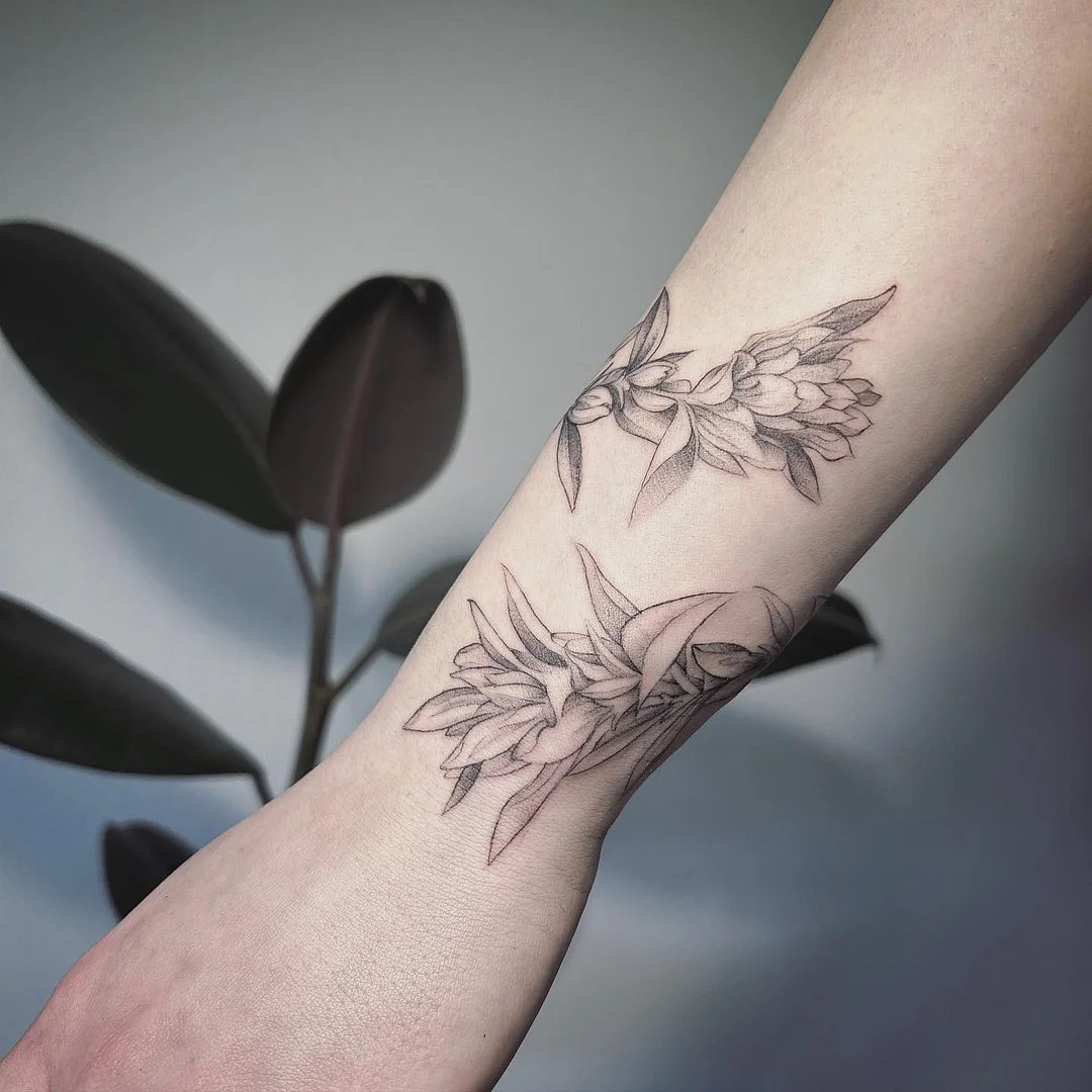 Delicate black and grey floral tattoo on forearm.